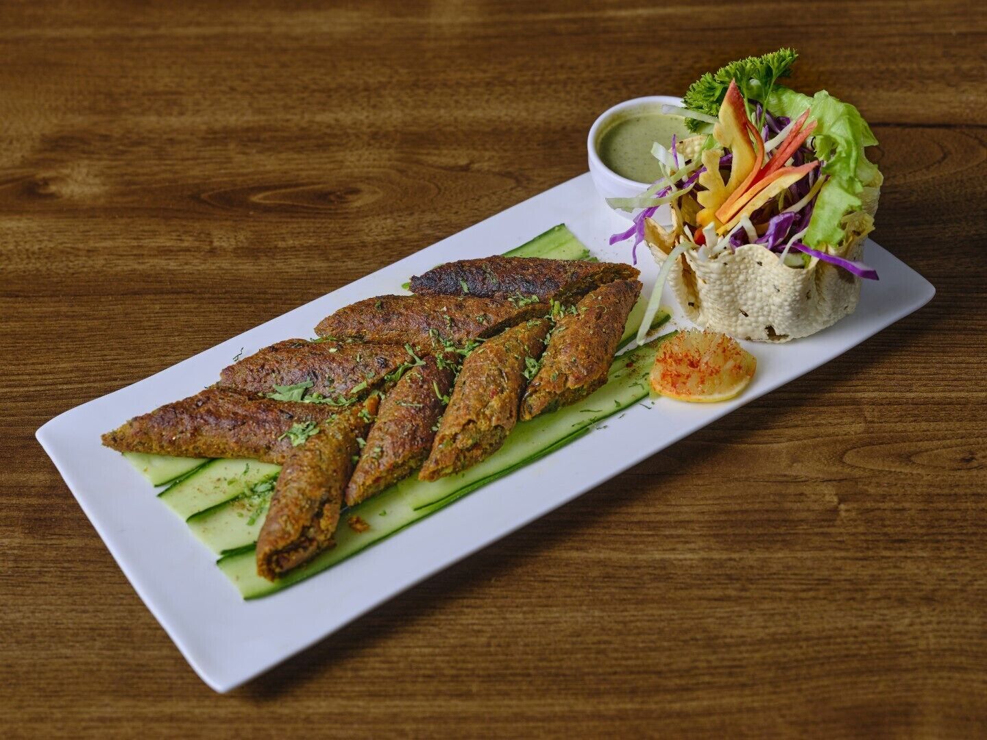 A white rectangular plate with grilled fish, cucumber slices, and a side salad with a green sauce.