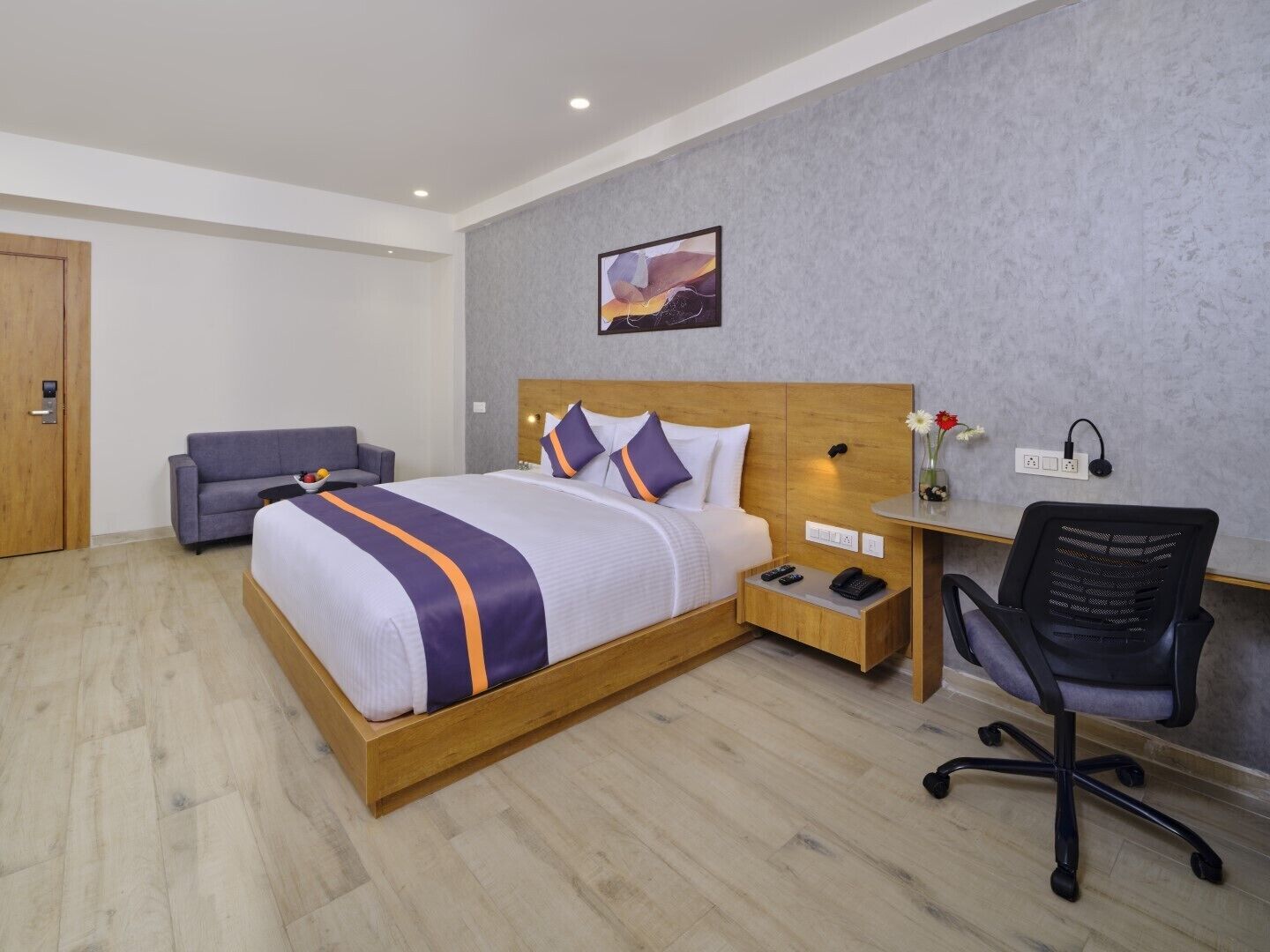 Una camera d'albergo con un letto grande, una scrivania con una sedia, un divano e una porta in legno.