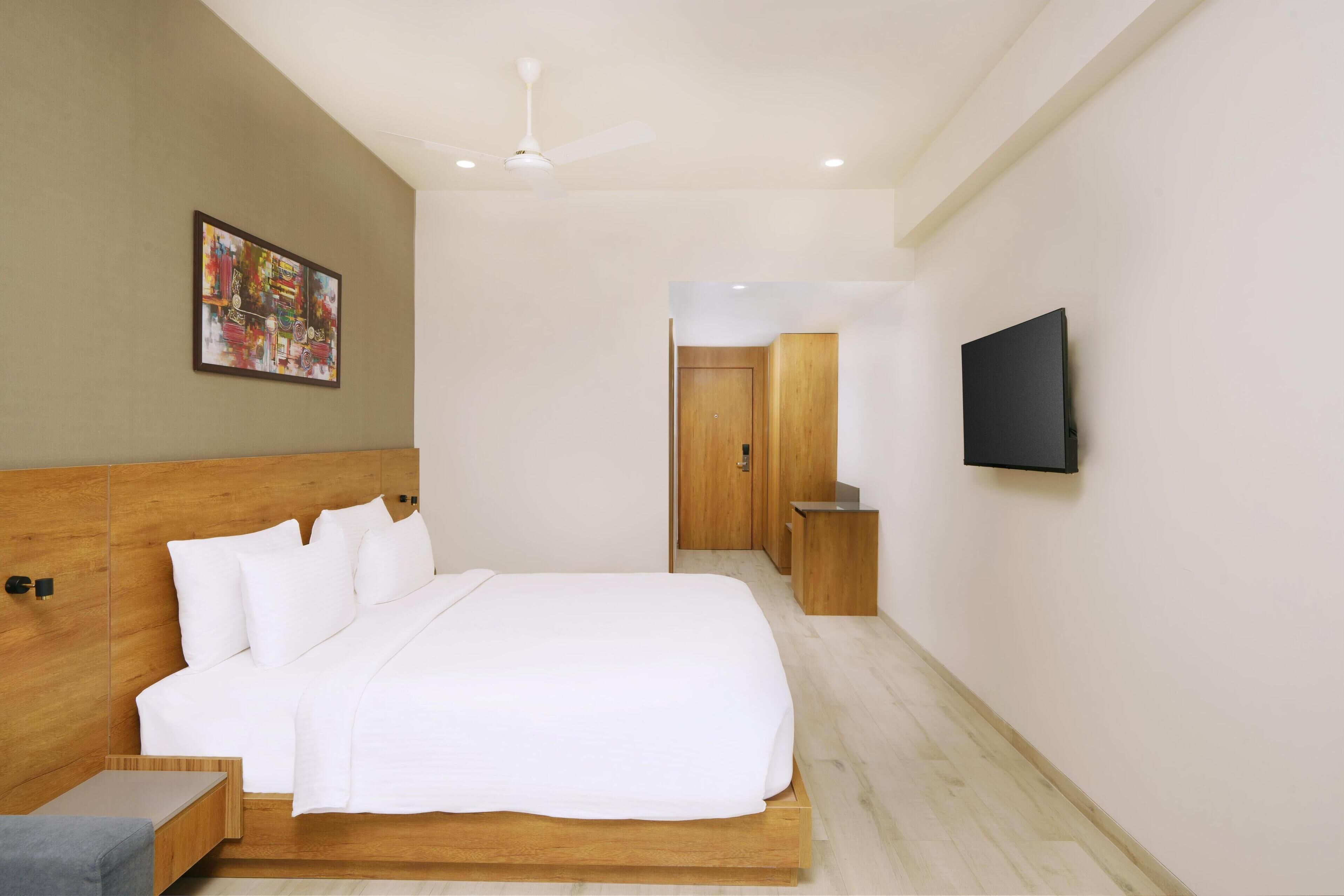 A modern hotel room with a large bed, a ceiling fan, a flat-screen TV, and a wooden headboard.