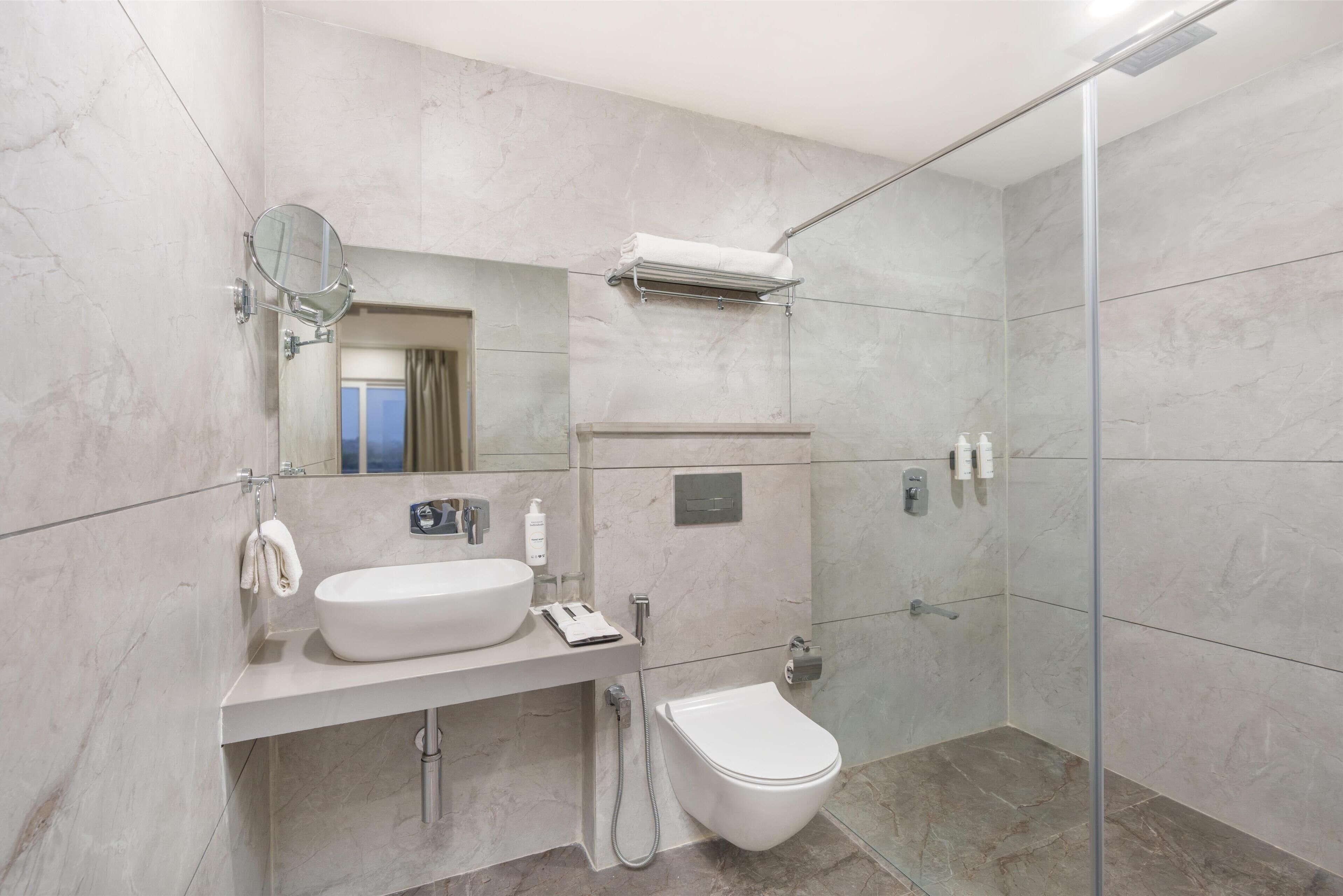 A modern bathroom with a sink, mirror, towel rack, and a glass-enclosed shower area.