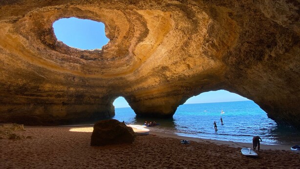 Formació rocosa natural amb una gran obertura, una platja de sorra i el mar visible a través de l'obertura.