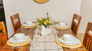 Une table de salle à manger en bois, dressée avec de l’assiette blanche, des bols et des verres, et agrémentée d’un arrangement floral jaune au centre.