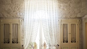 Una habitación con pared de piedra, dos puertas blancas con detalles verdes y una ventana con cortinas estampadas.