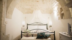Un dormitorio con techo de piedra, una cama con dosel, lámparas de noche, una mesita de noche y un televisor.
