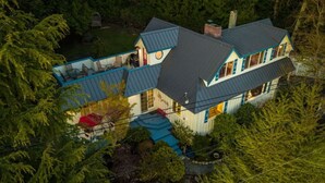 A two-story house with a blue roof, surrounded by dense trees. - NEWLY Renovated Anchor House | Rooftop Patio | Pet Friendly | 3min Walk to Beach (Freeland)