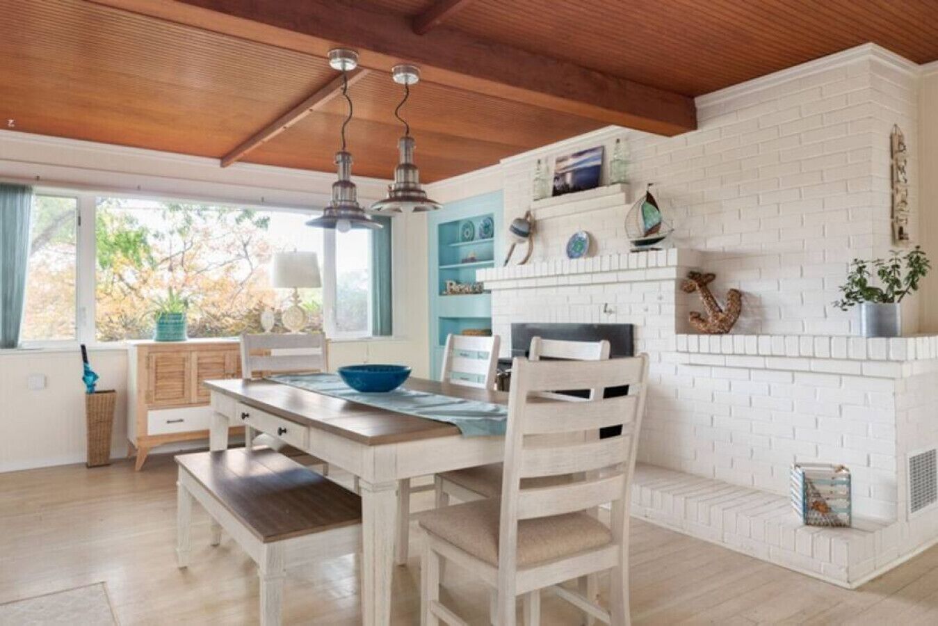 A dining area with a white table and chairs, a blue bowl, and a white brick fireplace with decorative items.