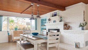 A dining area with a white table and chairs, a blue bowl, and a white brick fireplace with decorative items. - NEWLY Renovated Anchor House | Rooftop Patio | Pet Friendly | 3min Walk to Beach (Freeland)