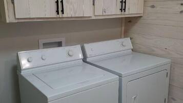 Une buanderie équipée de deux machines à laver et de deux sèche-linge à chargement frontal, tous deux de couleur blanche, avec des armoires en bois au-dessus et un plancher en bois.