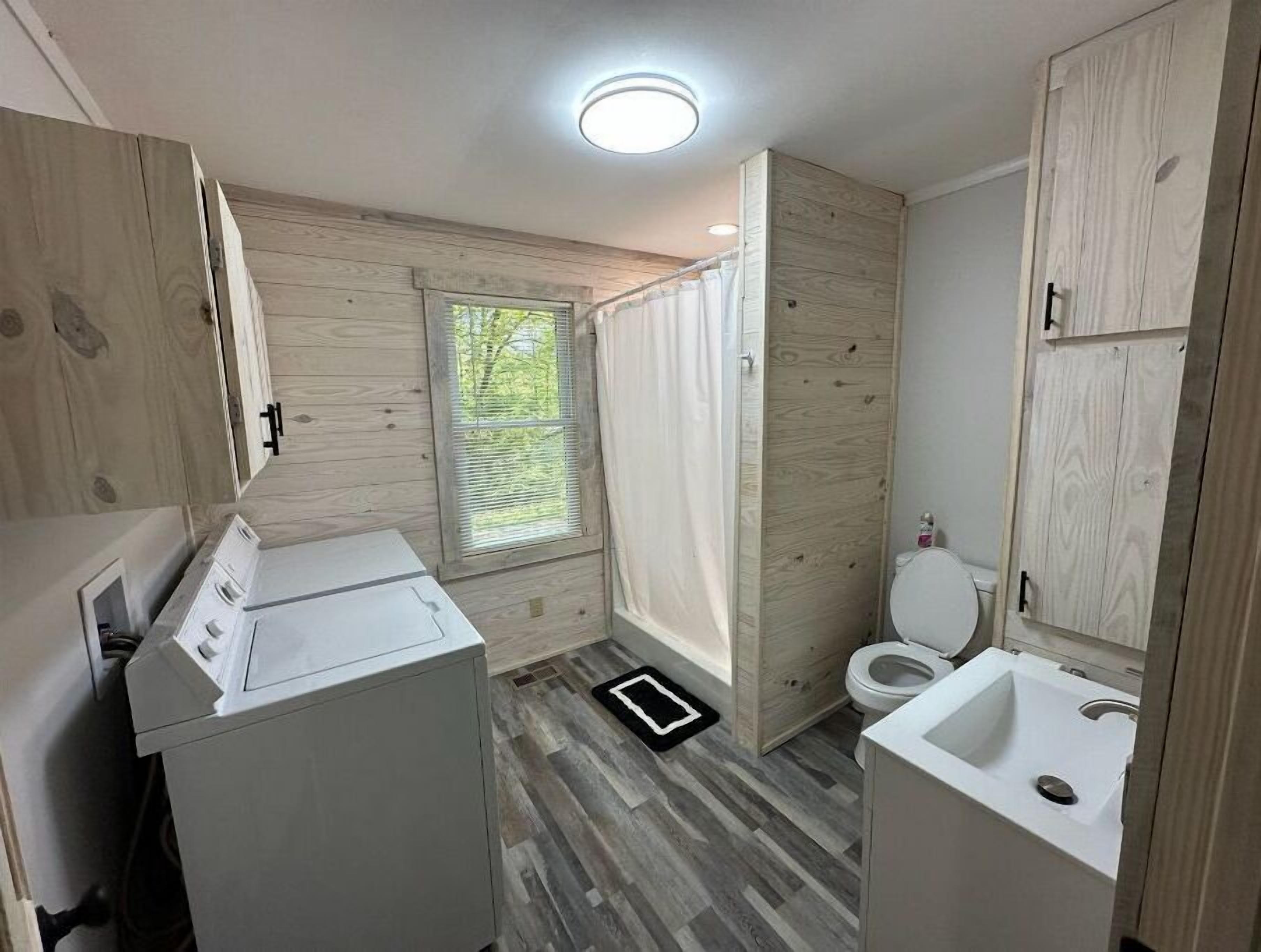 Een moderne badkamer met houten lambrisering, een ingebouwde wasmachine, een toilet en een wastafel.