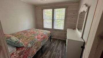 Une chambre à coucher comprenant un lit, une commode, un ventilateur de plafond et deux fenêtres.