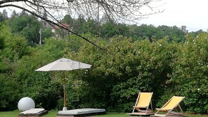 Uma área ao ar livre com gramado, um guarda-sol branco, duas cadeiras de descanso amarelas e um objeto esférico branco.