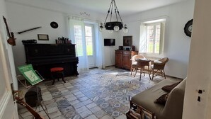Uma sala de estar com piano, televisão, lareira e área de jantar com cadeiras e mesa.