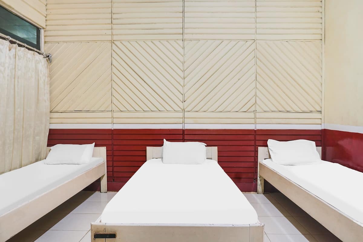 A hotel room with two single beds and a larger bed, all with white linens.