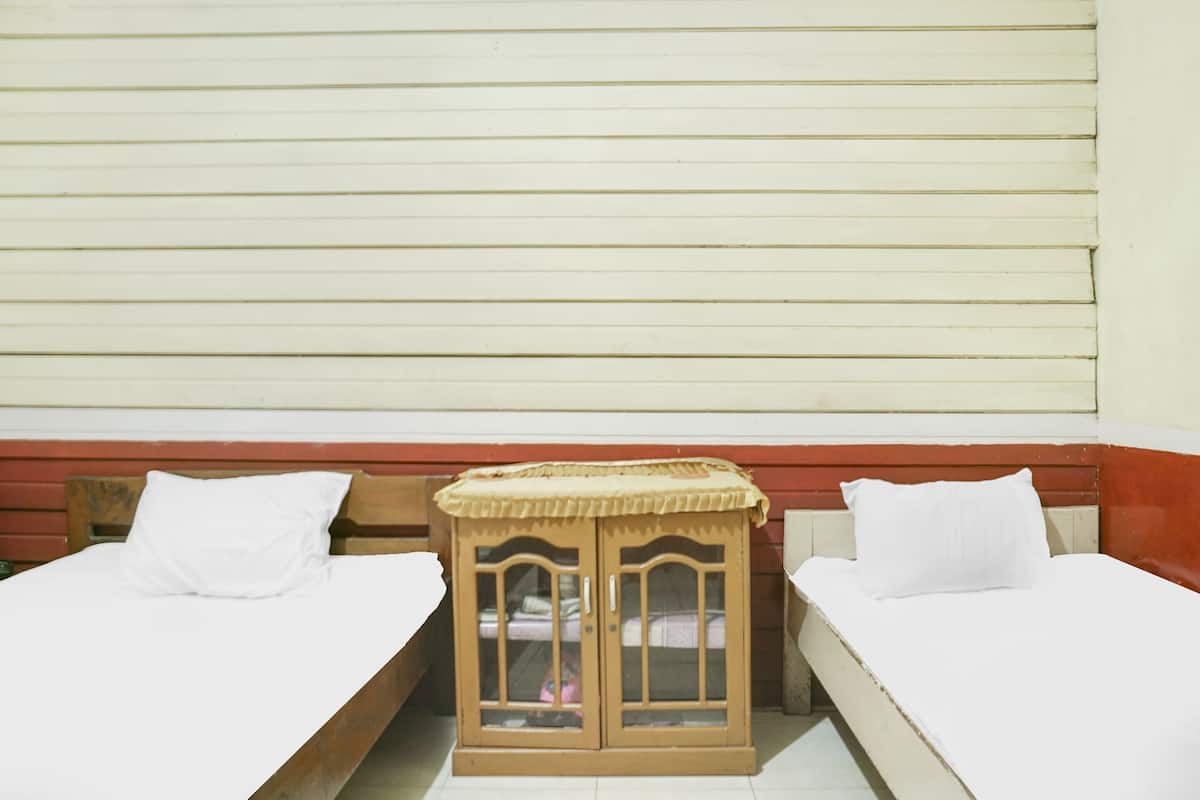 Two single beds with white linens, a wooden nightstand with a glass front, and a red and white wall.