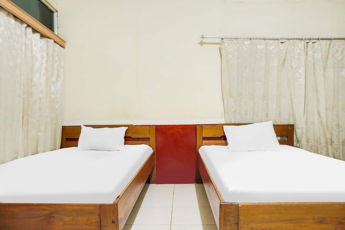 A room with two wooden beds, a red accent wall, and white curtains.