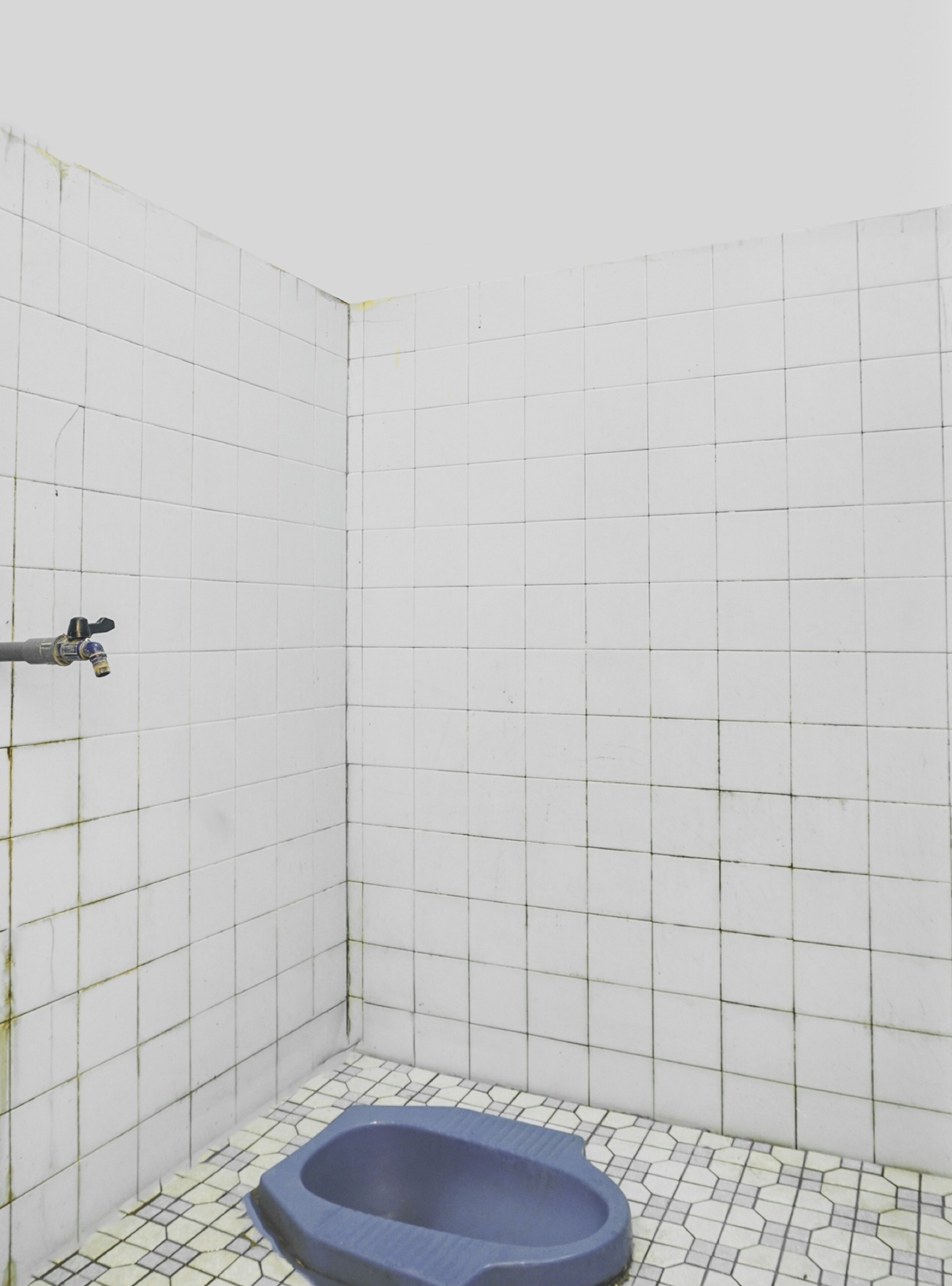 A small, tiled bathroom with a blue squat toilet and a faucet on the left.