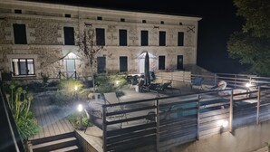 An outdoor pool area with lounge chairs and umbrellas, surrounded by stone buildings with multiple windows.