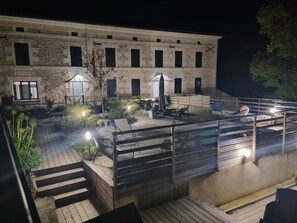 Un espace extérieur avec une piscine, des chaises longues et des parasols, entouré de bâtiments en pierre dotés de nombreuses fenêtres.