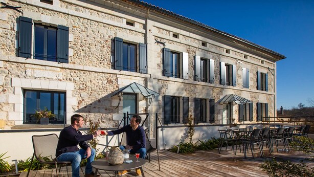A stone building with a patio area featuring outdoor seating and a glass-enclosed dining space.