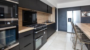 A modern kitchen with black cabinetry, a wooden countertop, a gas stove, an oven, and a stainless steel range hood.