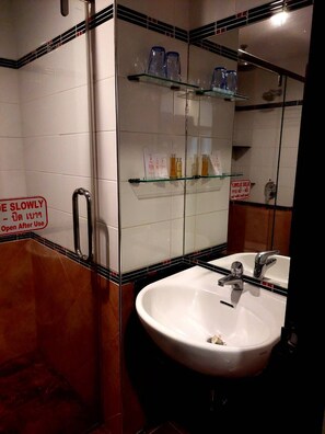 A bathroom with a white sink, two faucets, and a mirror above it. There are shelves with toiletries and a sign that says "Please slow down, open after use." - Soi 2 inn Pattaya (Pattaya)