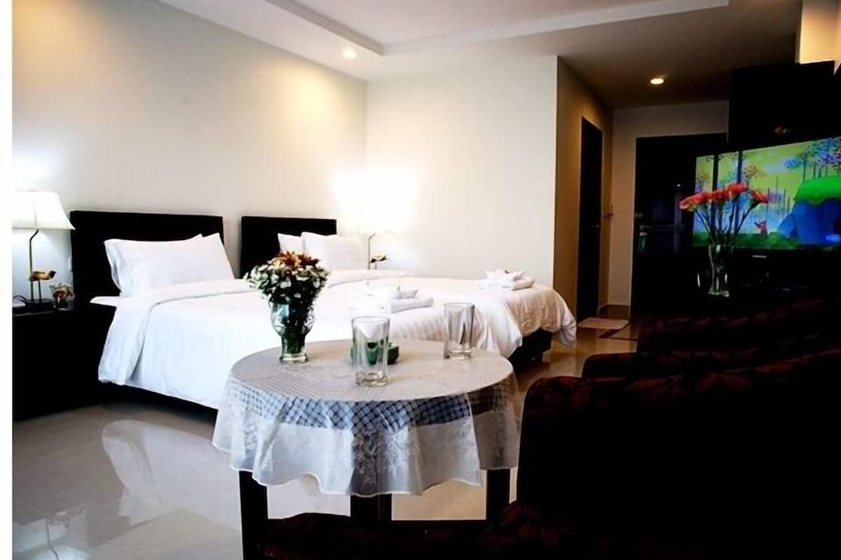 A hotel room with two beds, a TV, a round table with a vase of flowers, and a sofa.