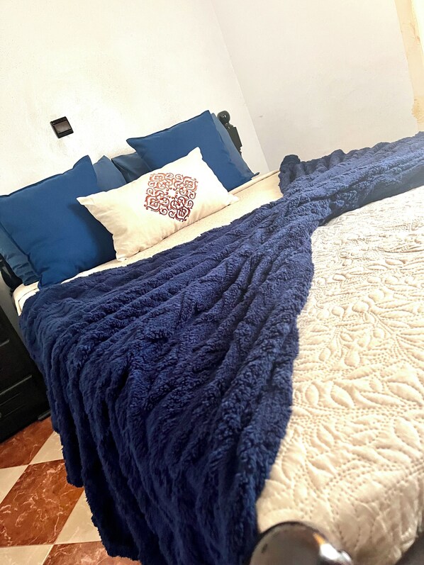 A bed with a blue blanket, a white pillow with a decorative pattern, and blue and white bedding.