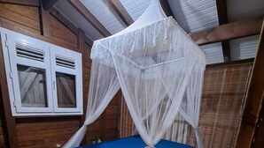 Quarto com estrutura de madeira e cama sob um dossel branco.
