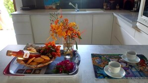 Uma bancada de cozinha com uma bandeja de comida, um vaso de flores e uma mesa posta com xícaras e pires.