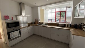A modern kitchen with white cabinets, a stainless steel range hood, a built-in oven, and a window with red frames. - Renovated town house in the heart of Arcachon (Arcachon)
