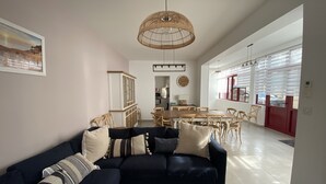 A modern living room with a dark blue sofa, wooden dining table, and chairs. There is a wicker ceiling light fixture and a clock on the wall. - Renovated town house in the heart of Arcachon (Arcachon)