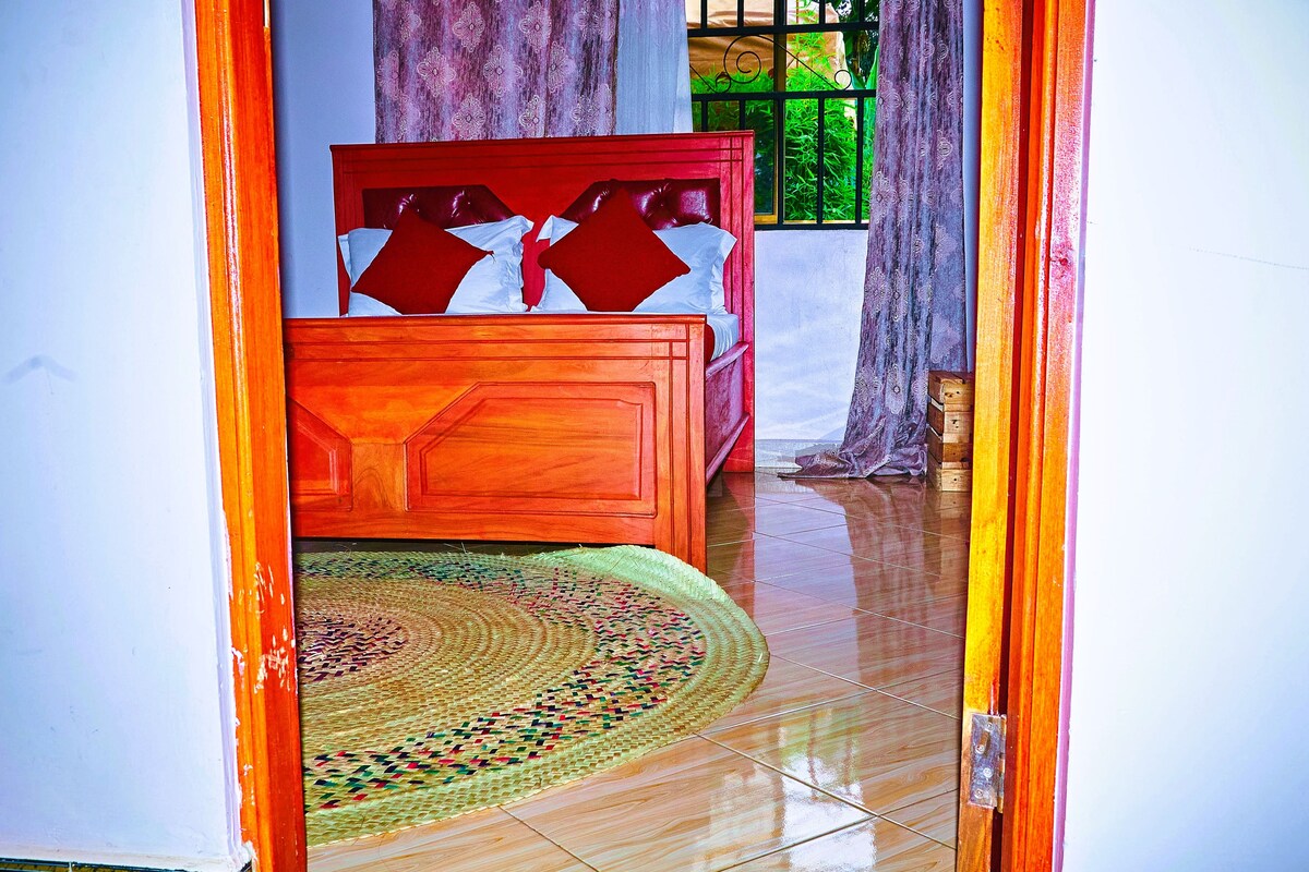 A bedroom with a wooden bed, a woven rug, and a window with bars.
