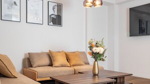 A modern living room with a sofa, a wooden coffee table, and a vase with flowers. There are framed pictures on the wall and a ceiling light fixture. - ART NAMBA HIGASHI  (Osaka)