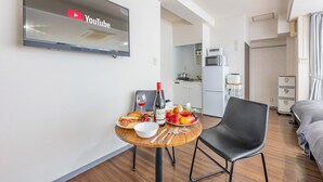 A modern hotel room with a flat-screen TV displaying YouTube, a dining table with breakfast, a black leather chair, and a kitchenette in the background. - ART NAMBA HIGASHI  (Osaka)