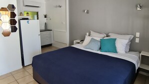 Un dormitorio con cama, mesita de noche, cómoda y una cocina visible a través de una puerta abierta.