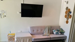 Una habitación con cama, sofá, una mesita con una botella de agua, un televisor montado en la pared y un adorno decorativo en la pared.