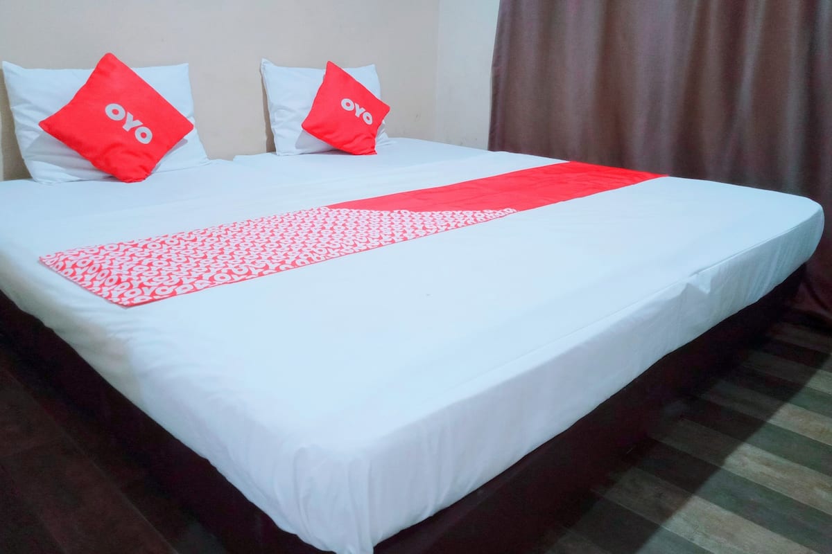 Una habitación de hotel con una cama bien hecha, dos almohadas con la palabra 'oyo' y un corredor rojo y blanco sobre la cama.
