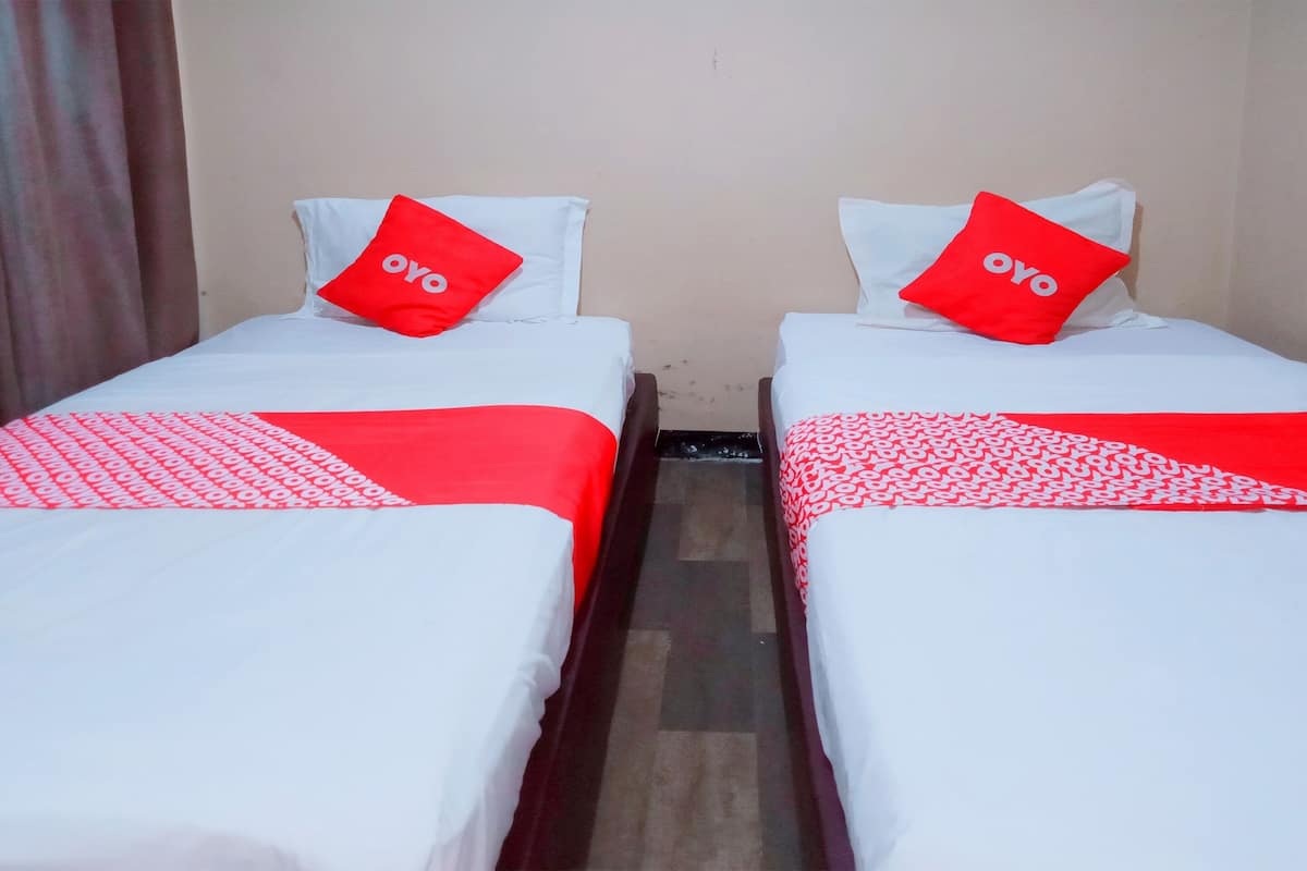 Dos camas individuales con ropa de cama blanca y roja, cada una con una almohada que dice "OYO".