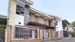 A multi-story residential building with a flat roof, a gated entrance, and a flag on the right side. - OYO Life 91626 Rr Kost Putri Syariah (Lumajang)