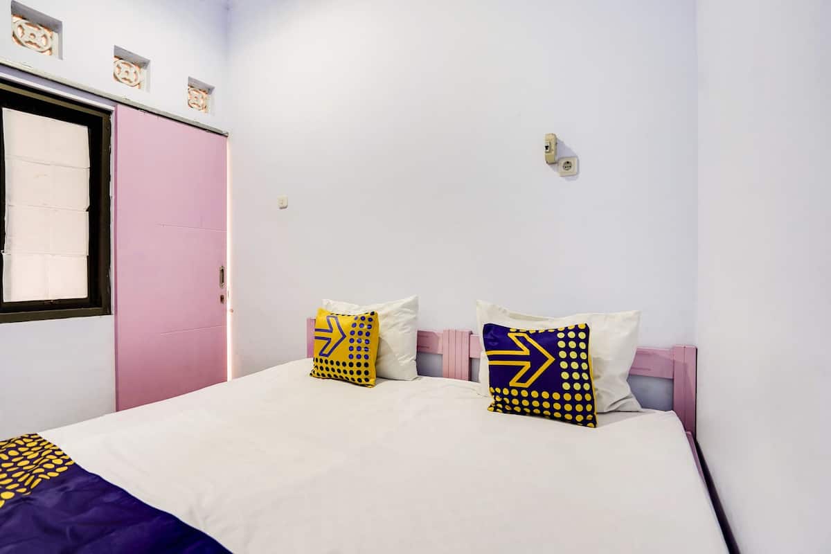 Un dormitorio con una cama, dos almohadas de diseños geométricos, una puerta rosa y una ventana con persianas.