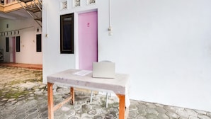 A room with a pink door, a table with a laptop, and a patterned floor. - OYO Life 91626 Rr Kost Putri Syariah (Lumajang)