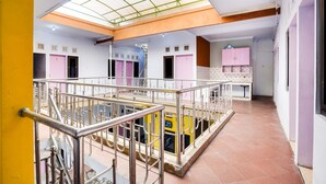 A hotel lobby with a central staircase, a glass ceiling, and a pink restroom area. - OYO Life 91626 Rr Kost Putri Syariah (Lumajang)