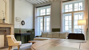 Ein Zimmer mit einem gebogenen Tisch, einer Couch, einem Sessel, einem Kamin und großen Fenstern.