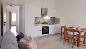 Une cuisine compacte avec des meubles blancs, un four encastré et un coin repas comprenant une table et des chaises en bois.