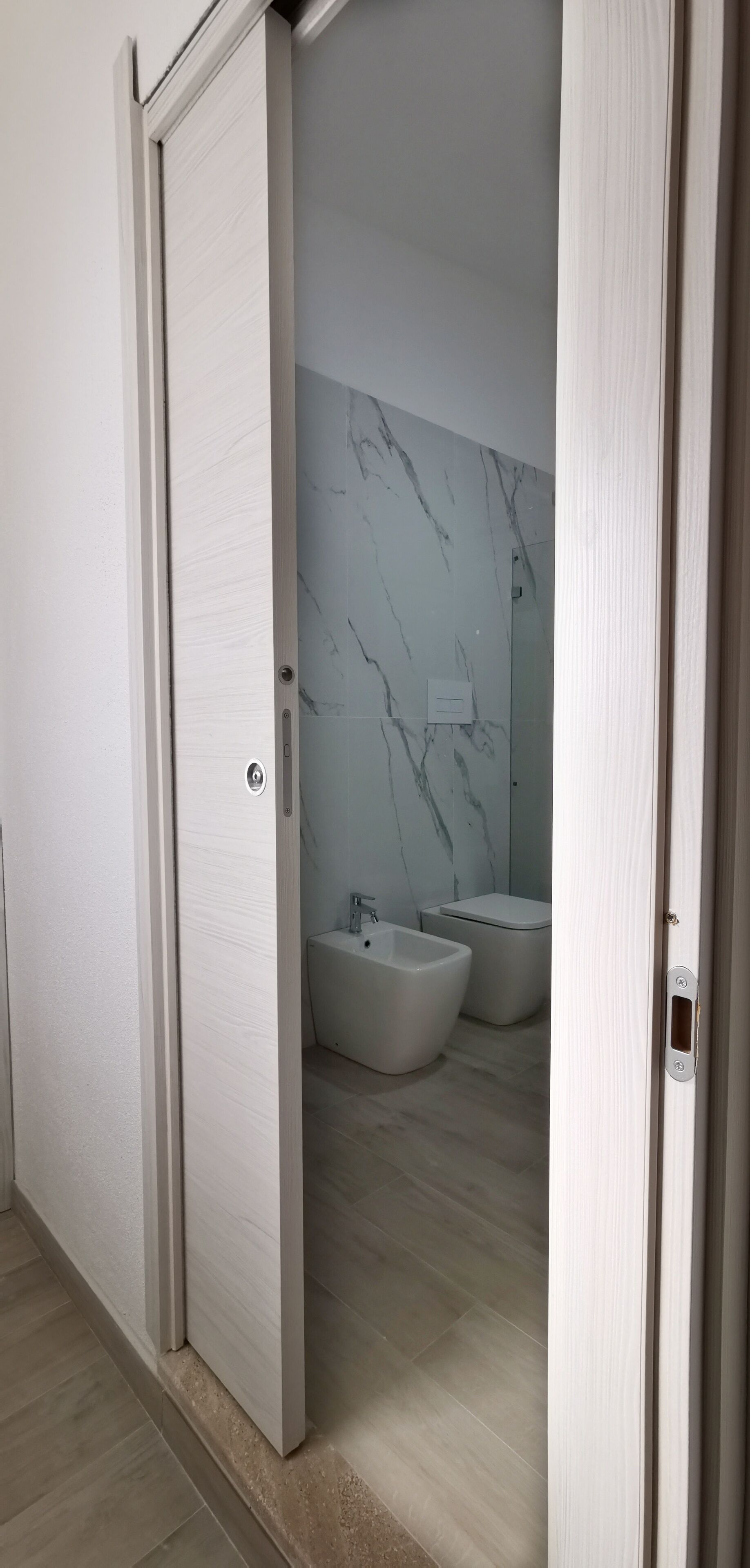 Ein modernes Badezimmer mit Marmorwand, einem Bidet und einer Toilette.