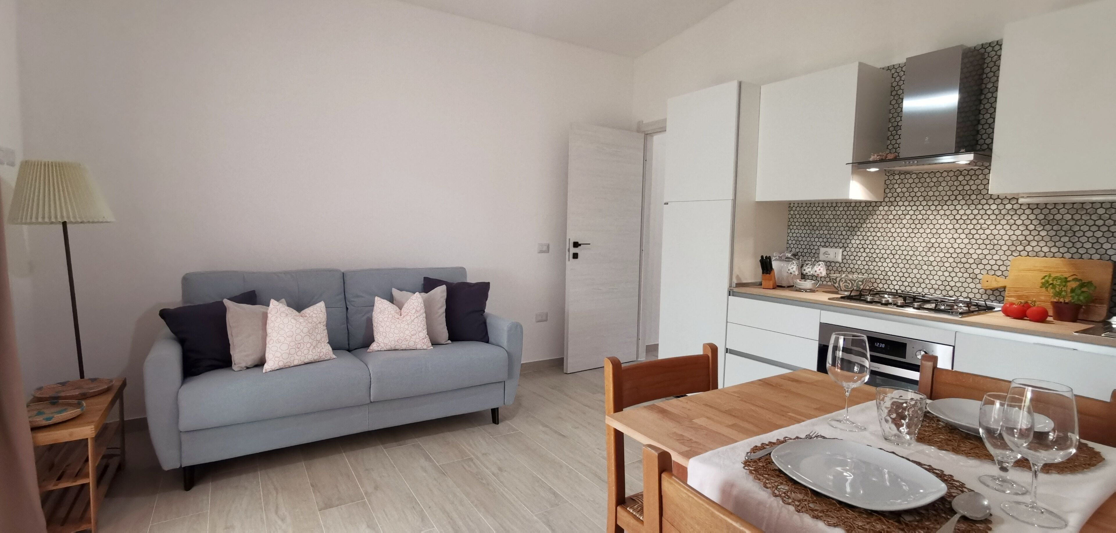 A modern kitchen with white cabinets, a grey sofa, and a dining table set for two.