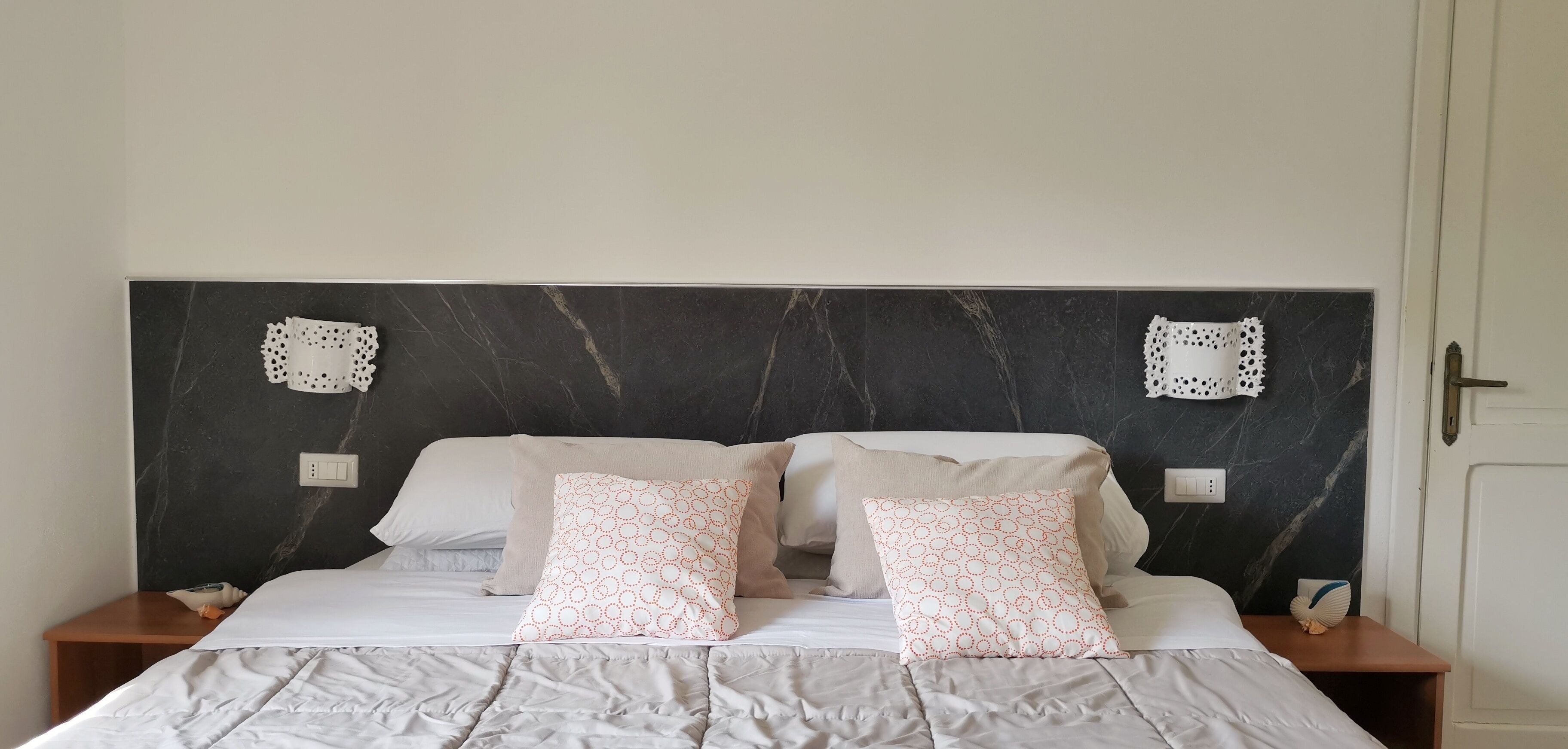 A neatly made bed with a grey duvet, two pillows with circular patterns, and a marble headboard.