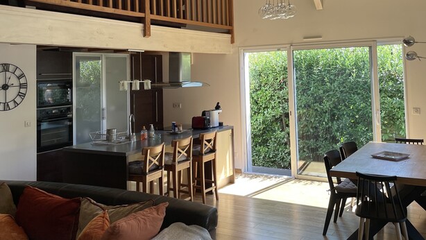 A spacious living area with a high ceiling, a balcony with wooden railings, a kitchen with modern appliances, and a dining area with a large table and chairs.