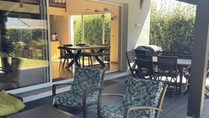 An outdoor patio area with wooden furniture, including a table and chairs, and a sliding glass door leading to a dining area.