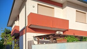 A two-story building with a balcony, a tiled wall with a mosaic design, and a small garden area.